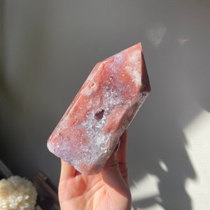 May include: A pink and white crystal point with a rough, textured surface. The crystal is shaped like a pyramid and has a pointed tip.