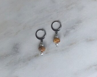 May include: A pair of silver hoop earrings with a brown and white bead dangle. The beads are round and have a natural stone look.