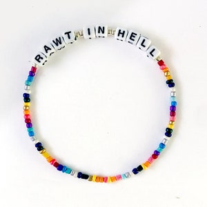 Op de afbeelding: Een kleurrijk kralenarmband met witte letterkralen die "RAW TIN HELL" spellen.
