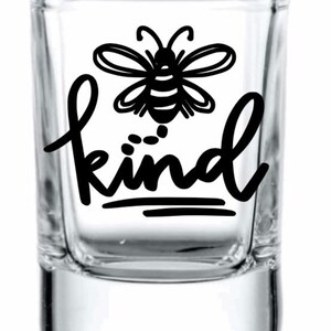 May include: A clear glass shot glass with a black bee and the word "kind" printed on it.