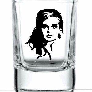 May include: A clear glass shot glass with a black and white silhouette of a woman's face on the front.