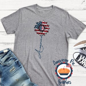 May include: Gray t-shirt with a red, white, and blue sunflower design and the word "America" written vertically down the stem. The shirt is from American Pie Graphics.