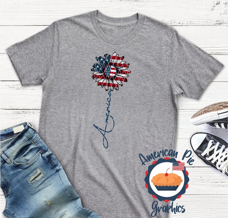 May include: Gray t-shirt with a red, white, and blue sunflower design and the word "America" written vertically down the stem. The shirt is from American Pie Graphics.