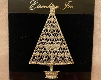 May include: Silver Christmas tree brooch with clear rhinestones and the text "Eisenberg Ice" on a black background.