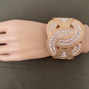 May include: Gold-tone cuff bracelet with a knot design and clear rhinestones.