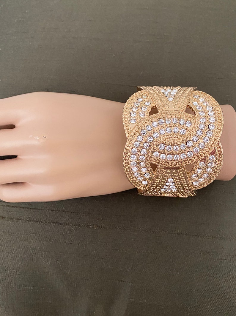 May include: Gold-tone cuff bracelet with a knot design and clear rhinestones.