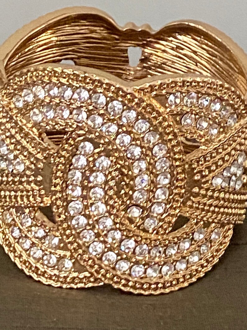 May include: A gold-toned bracelet with a knot design and clear rhinestones.
