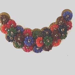 Può includere: Una spilla floreale decorativa con un design curvo. La spilla è adornata con piccoli fiori di tessuto colorati nelle tonalità del rosso, verde, blu e marrone, su una base dorata. I fiori hanno piccoli accenti color argento.