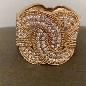 May include: A gold-toned bangle bracelet with a knot design and clear rhinestones.