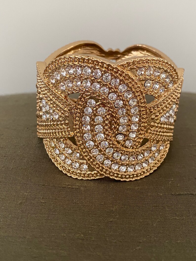 May include: A gold-toned bangle bracelet with a knot design and clear rhinestones.