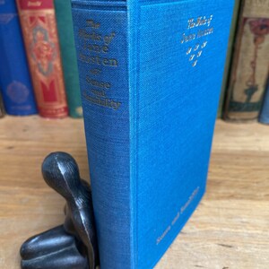 May include: A blue hardcover book titled "The Works of Jane Austen" with the words "Sense and Sensibility" printed in gold on the spine. The book is propped up by a black metal bookend shaped like a person.