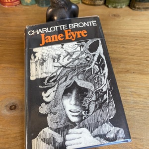 Peut inclure: Un livre broché noir et blanc avec le titre "Charlotte Bronte Jane Eyre" sur la couverture. La couverture présente une illustration en noir et blanc d'un visage de femme avec un arbre qui pousse hors de sa tête.