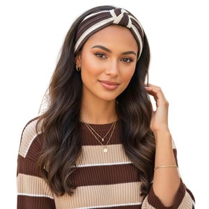 May include: A brown and white striped knotted headband. The headband is worn by a person with dark hair. The person is also wearing a brown and beige striped sweater and gold jewellery.