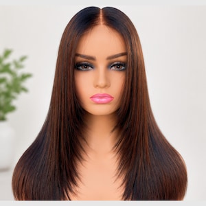 May include: A straight, shoulder-length wig featuring a dark brown root transition that blends into a lighter, warm chestnut brown tone. The hair is styled with a center part and subtle face-framing layers that taper toward the ends.