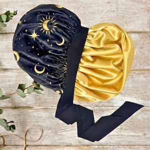 May include: A two-toned satin bonnet. One side is navy blue with gold celestial designs, including moons, stars, and suns. The other side is gold. A black band and tie complete the design. The bonnet is likely for hair protection.
