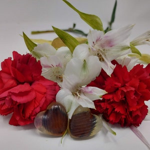 Op de afbeelding: Twee hartvormige harsversieringen met bruine en witte swirls, omringd door rode anjers en witte alstroemeria bloemen.