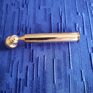May include: A gold-colored metal pipe with a round, ball-shaped end. The pipe is about 6 inches long and has a smooth, polished finish.