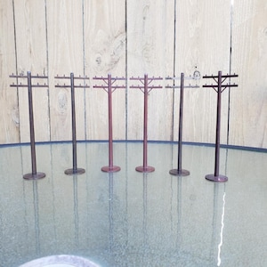 May include: Six brown wooden miniature utility poles with crossbars and wires. The poles are arranged in a row on a glass surface.