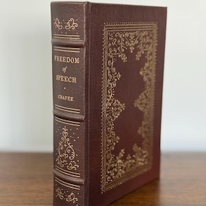 May include: A hardcover book with a dark brown leather cover. The title "FREEDOM OF SPEECH" is embossed in gold lettering on the spine. The cover features ornate gold filigree designs, creating a classic and elegant aesthetic.