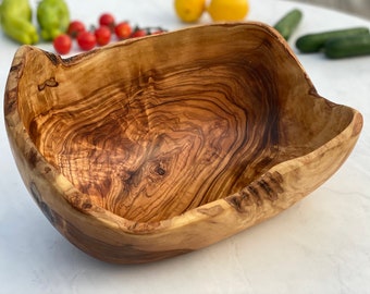 Könnte beinhalten: Eine große, rustikale Holzschüssel aus Olivenholz. Die Schüssel hat eine natürliche, unregelmäßige Form und eine satte braune Farbe mit komplexen Maserungen.