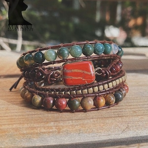 Könnte beinhalten: Ein mehrlagiges Armband mit braunem Lederband und verschiedenen bunten Edelsteinperlen. Das Armband hat einen quadratischen roten Stein mit goldenen Adern.