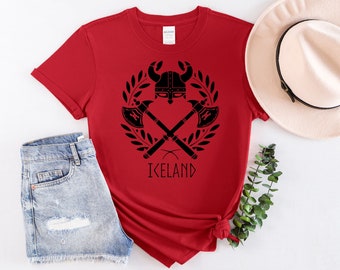 May include: Red t-shirt with a black graphic of a Viking helmet with crossed axes and a laurel wreath. The text "ICELAND" is below the graphic.
