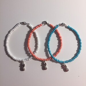 May include: Three beaded bracelets with pineapple charms. The bracelets are white, coral, and turquoise.