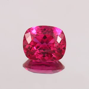 Op de afbeelding: Een levendige roze edelsteen met een kussen-slijpvorm. De edelsteen is gefacetteerd en heeft een hoge mate van glans.