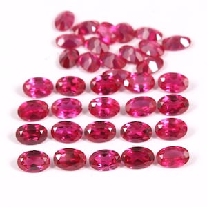 May include: A collection of oval-shaped, bright red gemstones. The gemstones are arranged in rows, with the top row having a few more gemstones than the rows below.