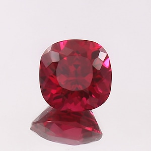 May include: A deep red gemstone with a cushion cut. The gemstone is faceted and has a high polish.