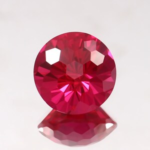 May include: A bright red round gemstone with a faceted cut. The gemstone is reflecting light and has a shiny finish.