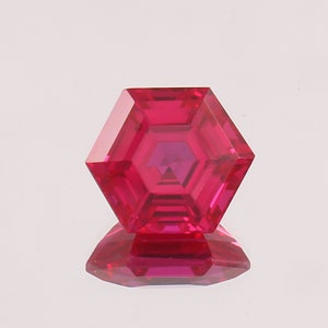 May include: A bright red hexagonal gemstone with a faceted design. The gemstone is cut in a unique shape with multiple facets.