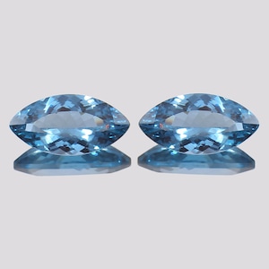 Op de afbeelding: Twee blauwe topaas edelstenen in marquise-vorm, beide met een briljant-slijpsel en een lichtblauwe kleur.