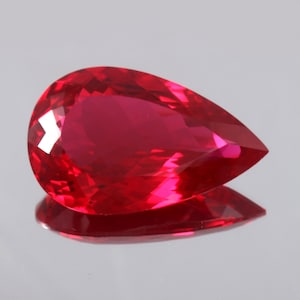 Könnte beinhalten: Ein leuchtend roter birnenförmiger Edelstein mit Facettenschliff.