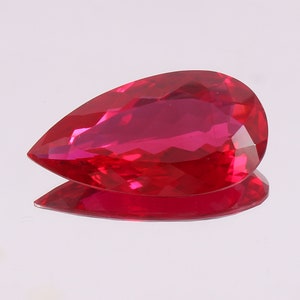 以下が含まれることがあります： 白の背景に置かれた、洋梨型の深い赤色のファセットカットの宝石