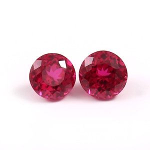 Pode incluir: Duas pedras preciosas redondas e facetadas de cor vermelha. As pedras preciosas estão sobre um fundo branco.