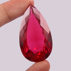 Könnte beinhalten: Ein großer, birnenförmiger, facettierter Edelstein in tiefroter Farbe.