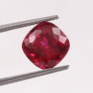 Puede incluir: Una piedra preciosa de talla cojín de color rojo intenso con muchas facetas.