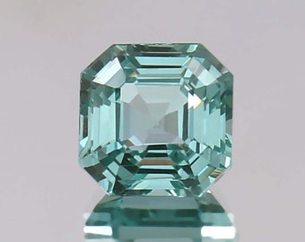 May include: A light blue, square-shaped gemstone with a faceted cut. The gemstone is reflecting light, showing its facets.