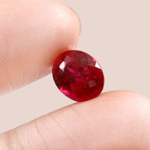 May include: A deep red oval-shaped gemstone with facets.
