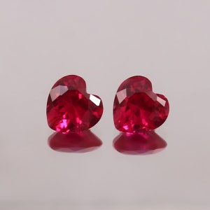 Puede incluir: Dos piedras preciosas de rubí en forma de corazón, cada una con un color rojo intenso y un corte facetado.