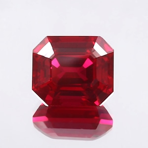 May include: A deep red emerald cut gemstone with a high polish.