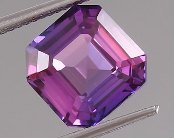 May include: A purple gemstone with a square emerald cut. The gemstone is held in tweezers.