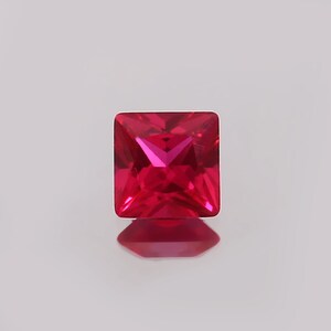 Puede incluir: Una piedra preciosa cuadrada de color rojo vibrante con un corte facetado.