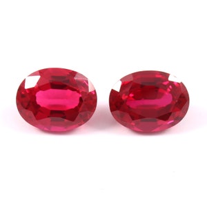 May include: Two oval-shaped, bright red gemstones. The gemstones are faceted and have a high polish.