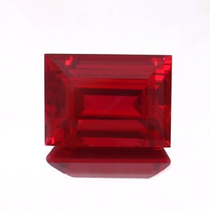 May include: A deep red emerald cut gemstone with a polished finish.