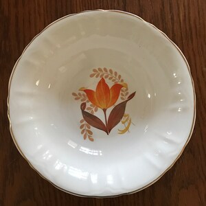 Könnte beinhalten: Weiße Keramikschüssel mit goldfarbenem Rand und einem Blumendesign mit einer orangefarbenen Tulpe mit braunen Blättern und Stielen.