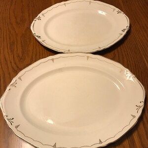 May include: Two white oval serving platters with gold trim and a delicate floral design. The larger platter is on top of the smaller platter.
