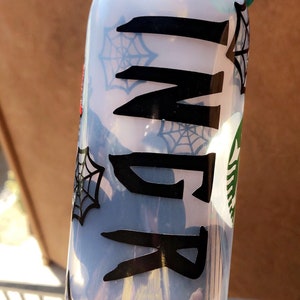 May include: A clear plastic water bottle with a black spiderweb design and the name "Ingrid" written in black lettering.