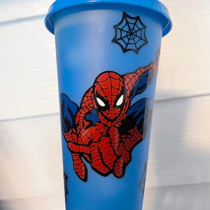 May include: A blue reusable cup with a Spider-Man design. The cup has a black spider web design and a red and blue Spider-Man character.